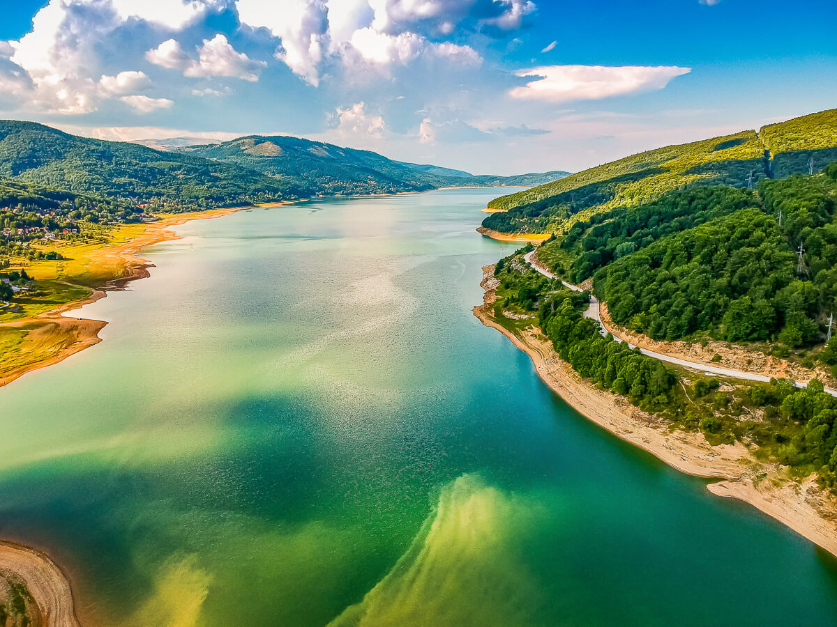 Aerial view of a winding river through a green valley under blue skies with distant hills