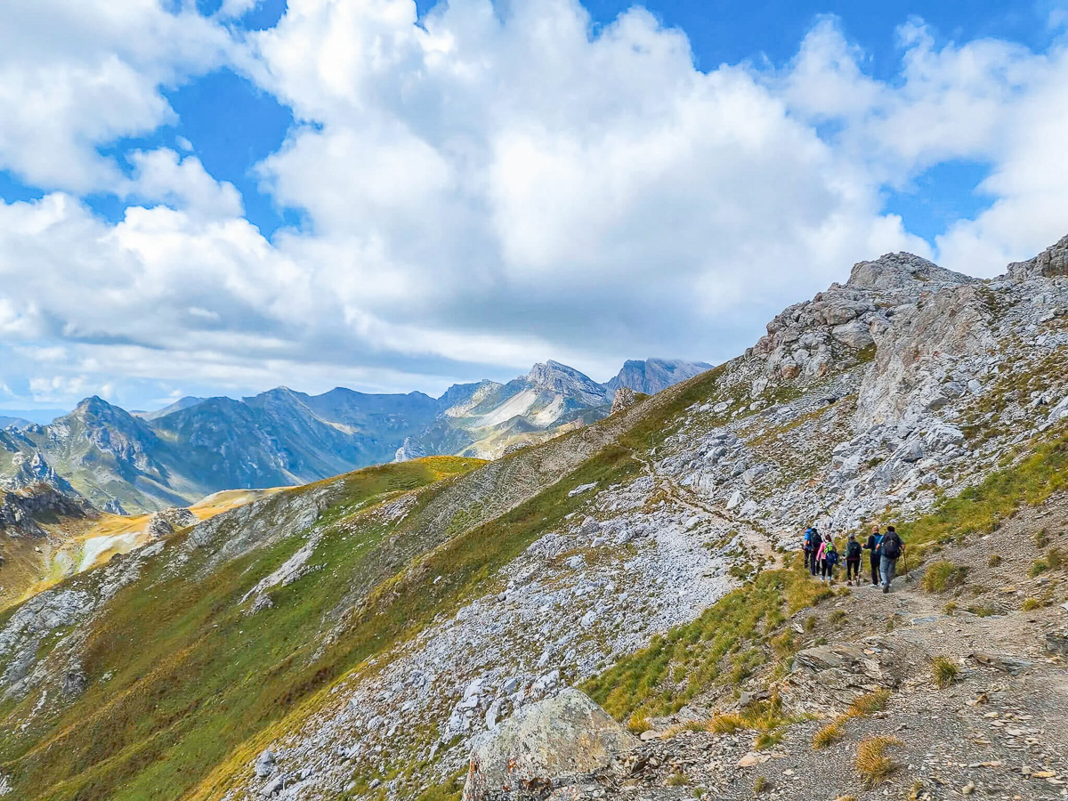 Women hiking along a rocky mountain ridge under a blue sky and clouds