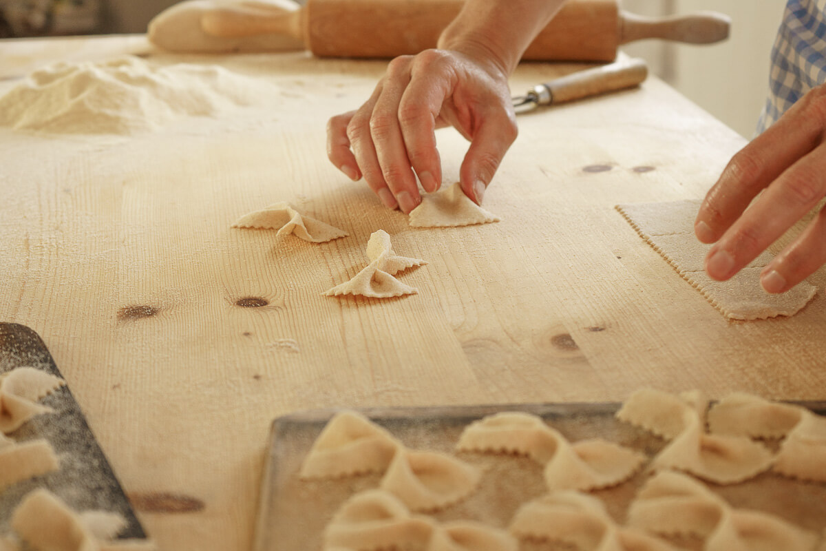 Women hand-cut pasta on a floured wooden table, preparing bite-sized shapes for cooking