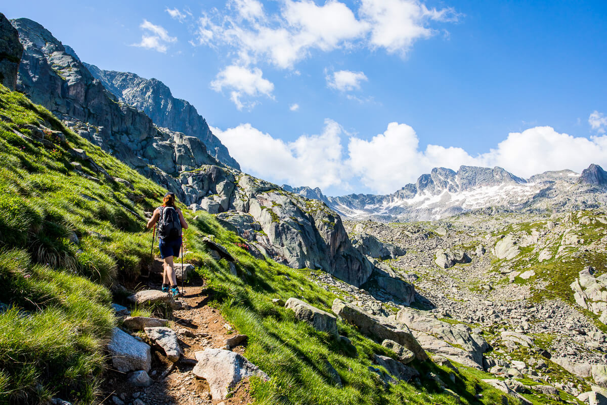 Woman hiking a rocky mountain trail in the Alps, with snow-capped peaks and green slopes in view