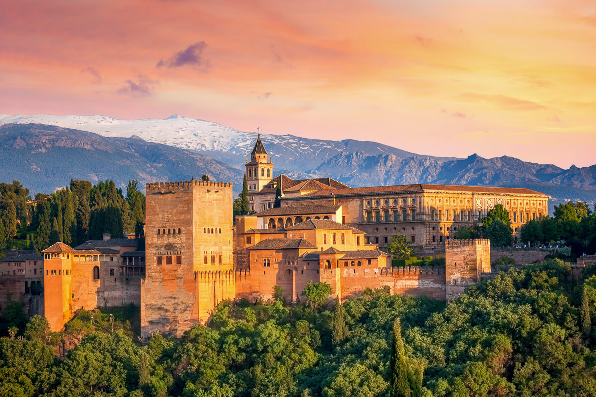Alhambra palace fortress in Granada, Spain, at sunset with snow-capped mountains in the background