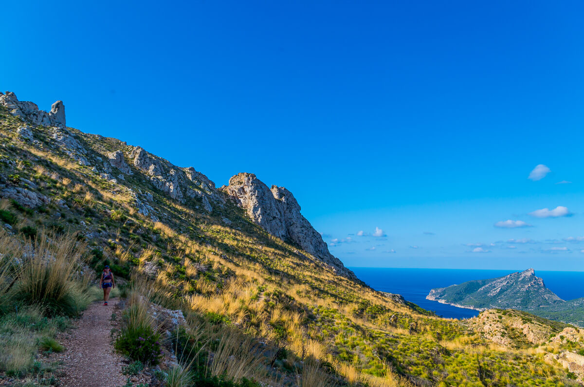 Woman hiking along a coastal cliffside trail with sea views and rocky mountains in the distance