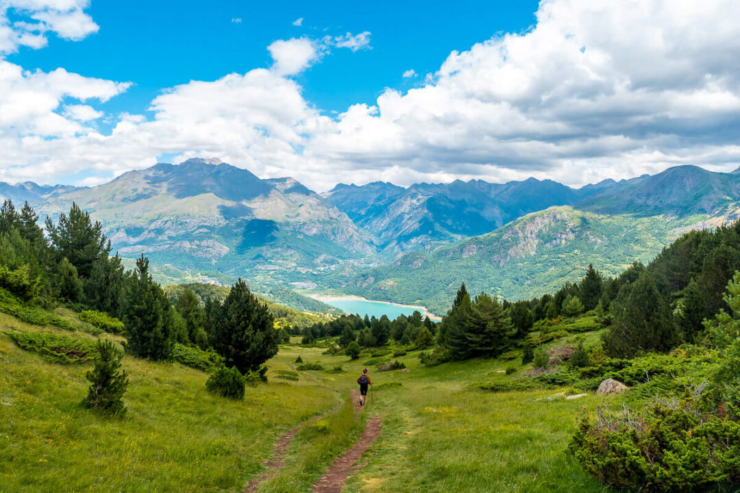 Woman hiking along a trail through a green mountain valley under a blue sky