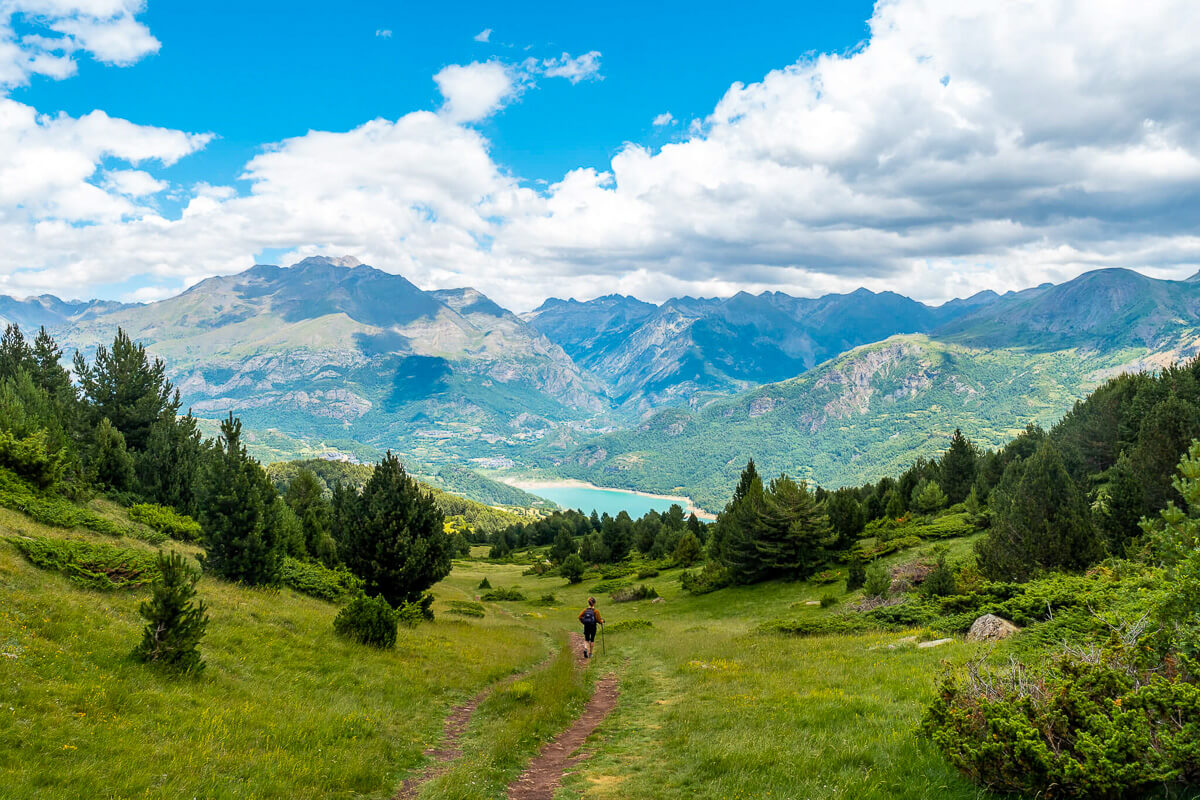 Woman hiking along a trail through a green mountain valley under a blue sky