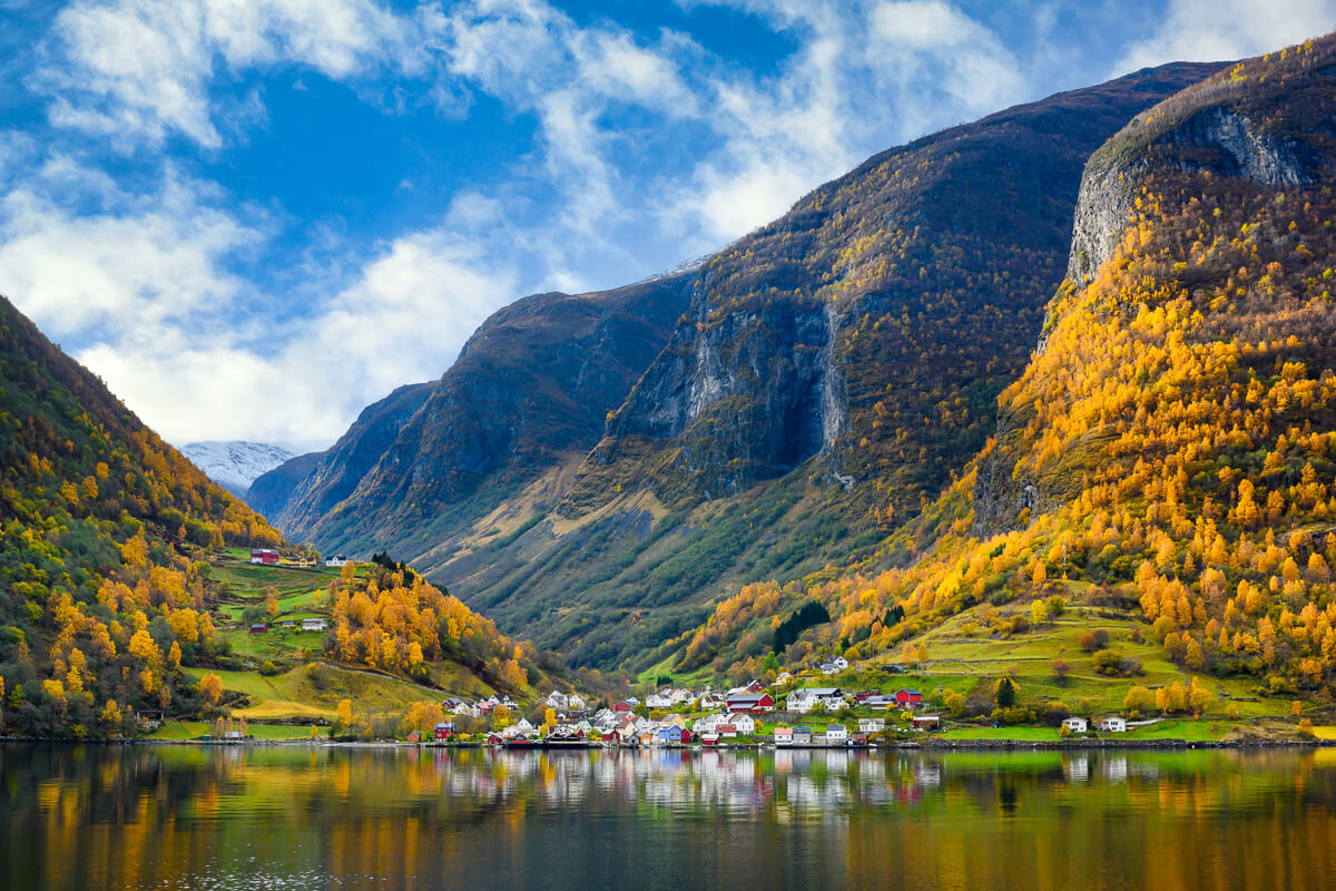 Lakeside mountain valley village with reflections and autumn trees under a blue sky