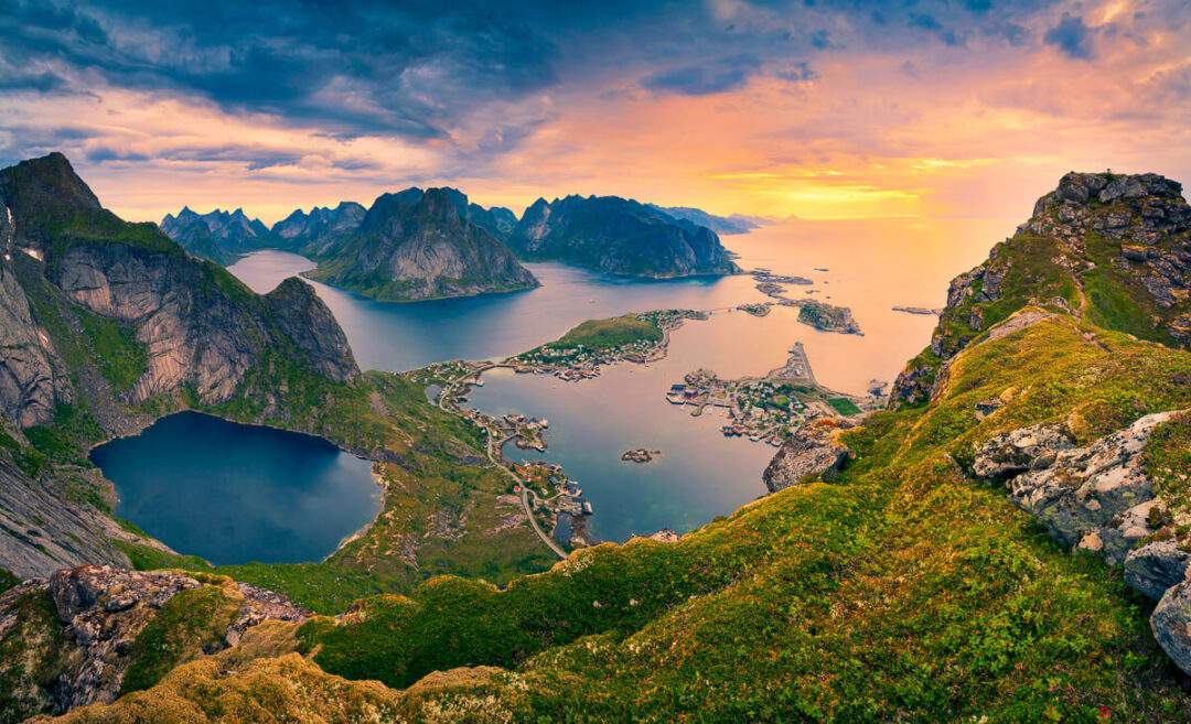Coastal fjord landscape with rocky mountains and green hills at sunset, calm sea and small boats.