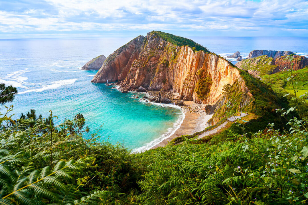 Clifftop coastline with turquoise sea and sandy beach at sunset, viewed from lush green hillside in Europe