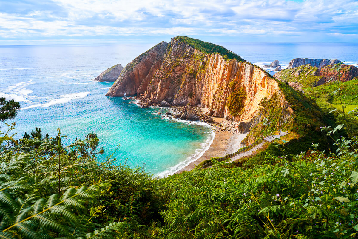 Clifftop coastline with turquoise sea and sandy beach at sunset, viewed from lush green hillside in Europe