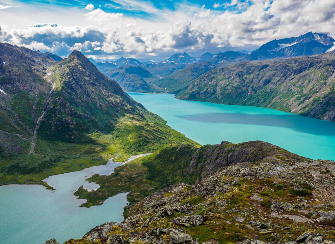 Turquoise glacier lake in a mountain valley, aerial landscape view over rugged peaks and forests