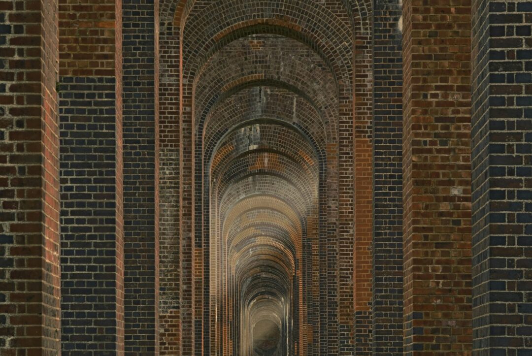 Long arched brick corridor walkway with repeating brick arches and columns in a tunnel-like passage