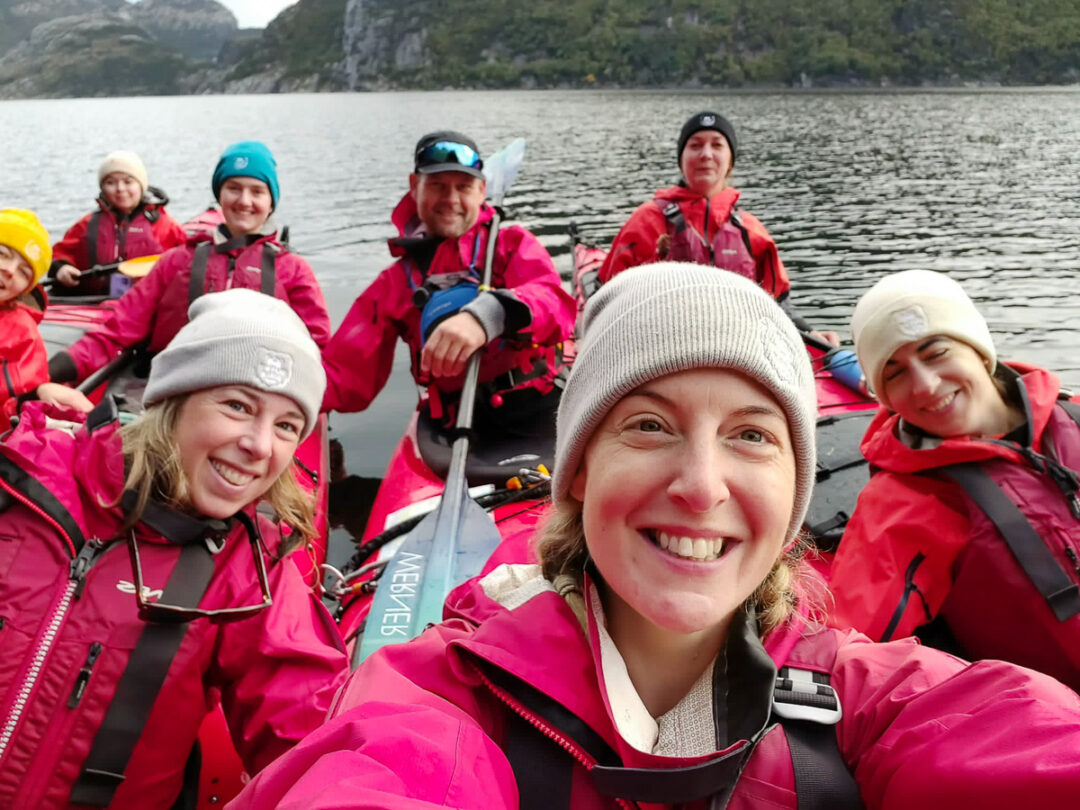 Women in bright pink life jackets on a boat trip on a lake with mountains in the background.