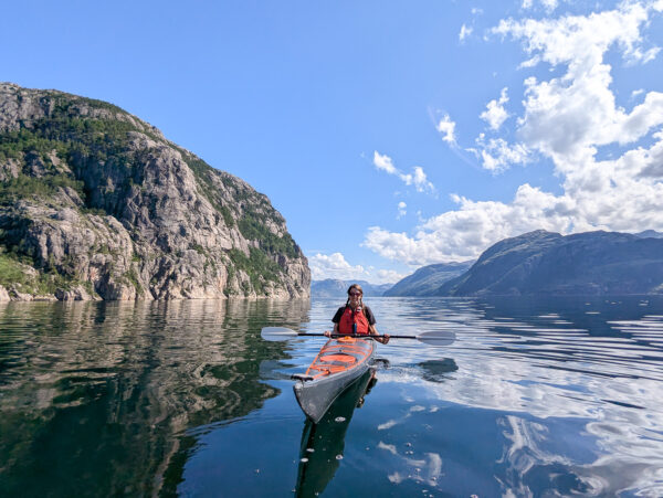 Woman kayaking on a calm lake, surrounded by mountains and rocky cliffs