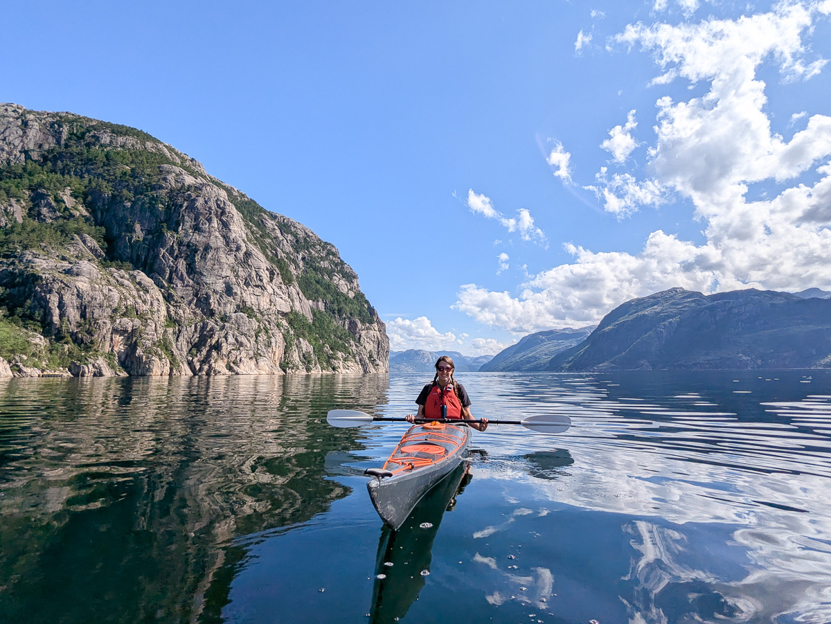 Woman kayaking on a calm lake, surrounded by mountains and rocky cliffs