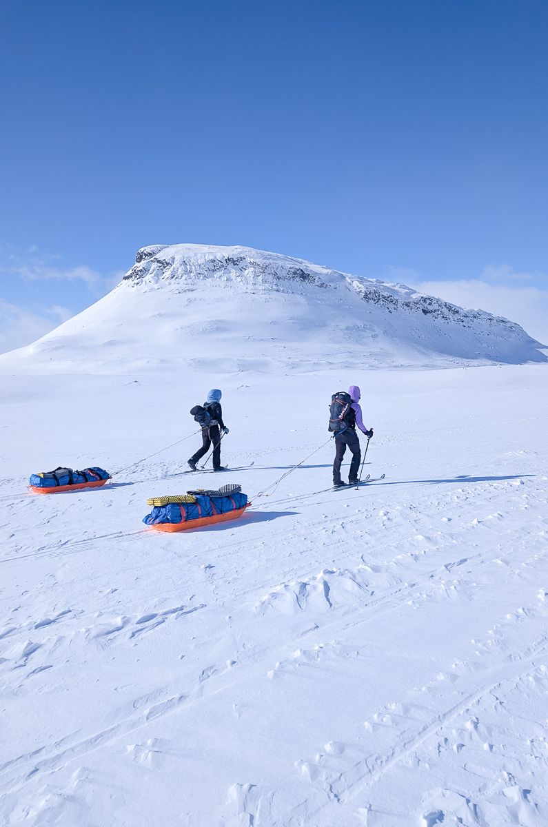 Women ski-touring hut-to-hut trek across Arctic snow toward a mountain summit