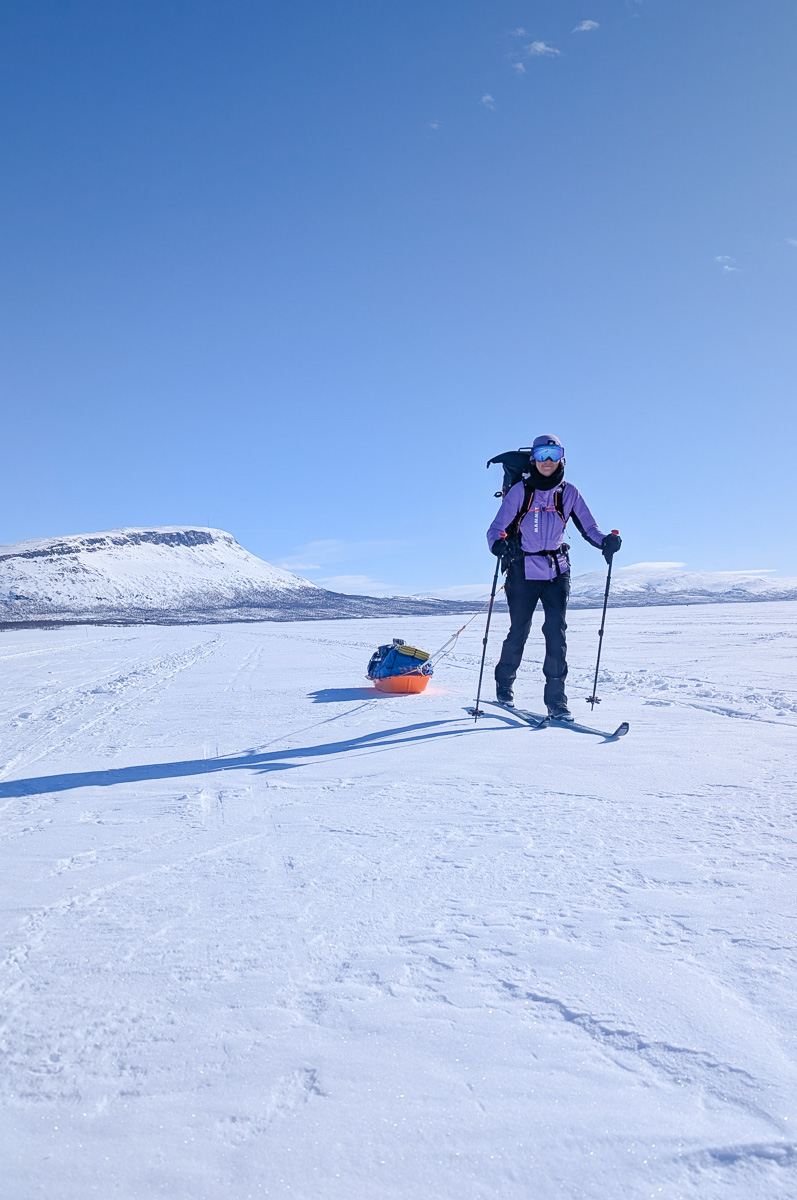Women cross-country skiing across a snowy Arctic landscape with poles and a backpack
