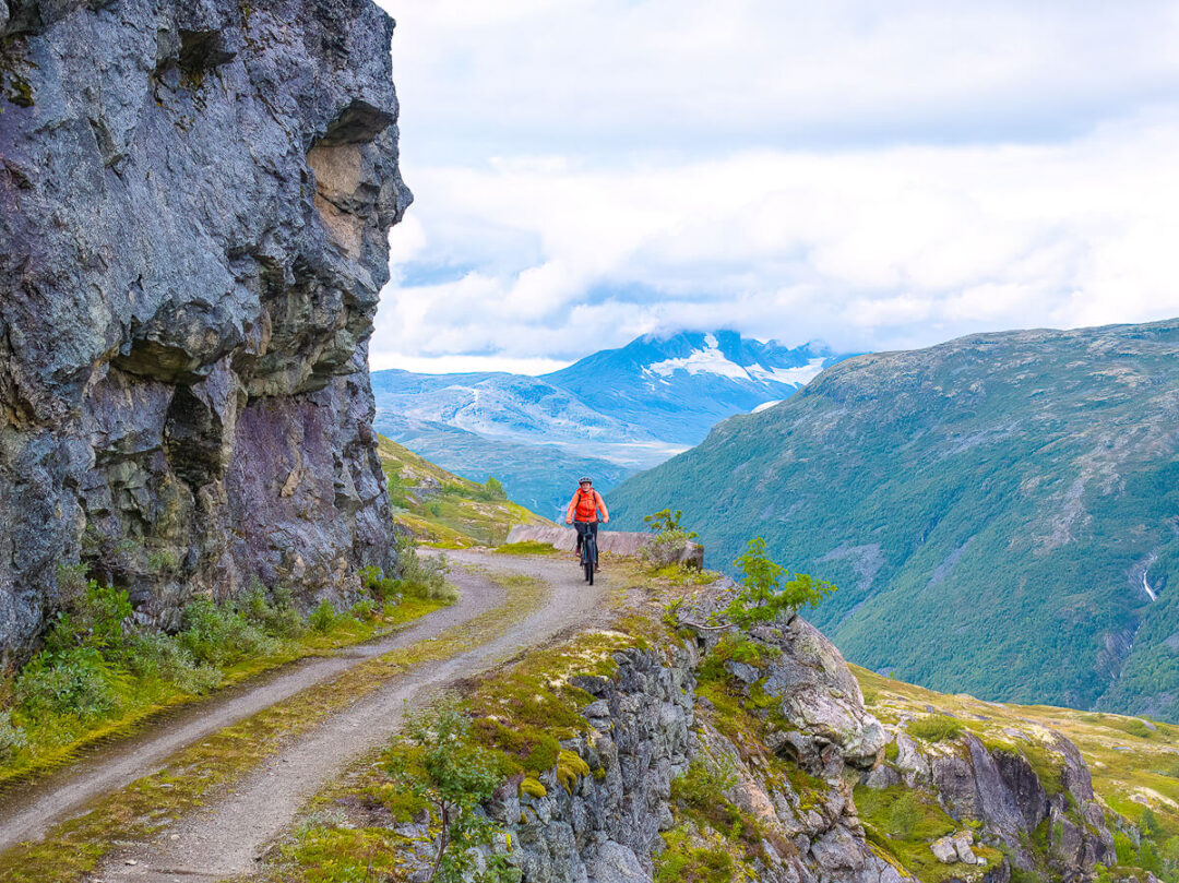 Woman hiking along a rocky mountain trail overlooking a valley and distant peaks
