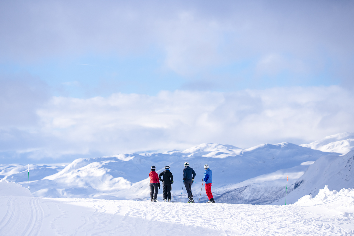 Women hiking on snowy ski slopes with mountain peaks under a blue sky