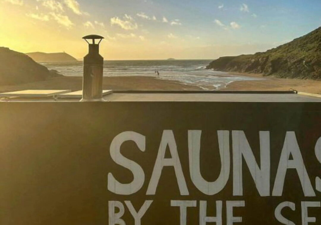 Sauna sign reading “SAUNA BY THE SEA” overlooking the sea at sunset