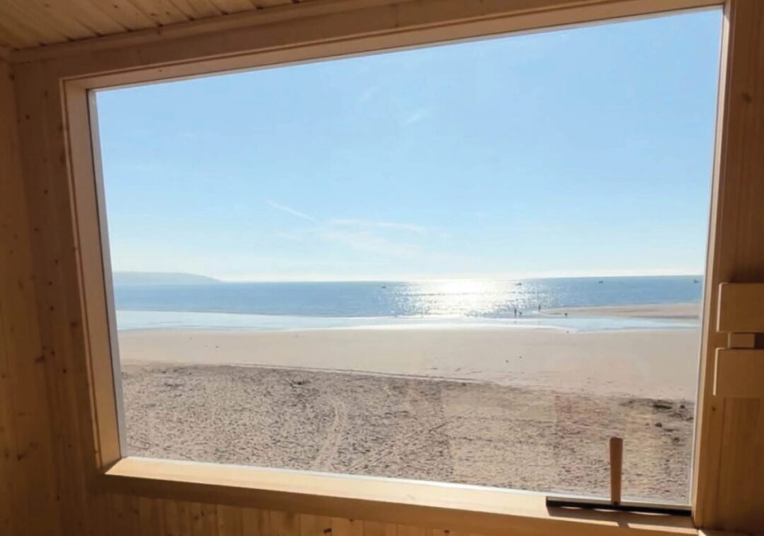 View from a wooden sauna window onto a sandy beach and sea in the UK