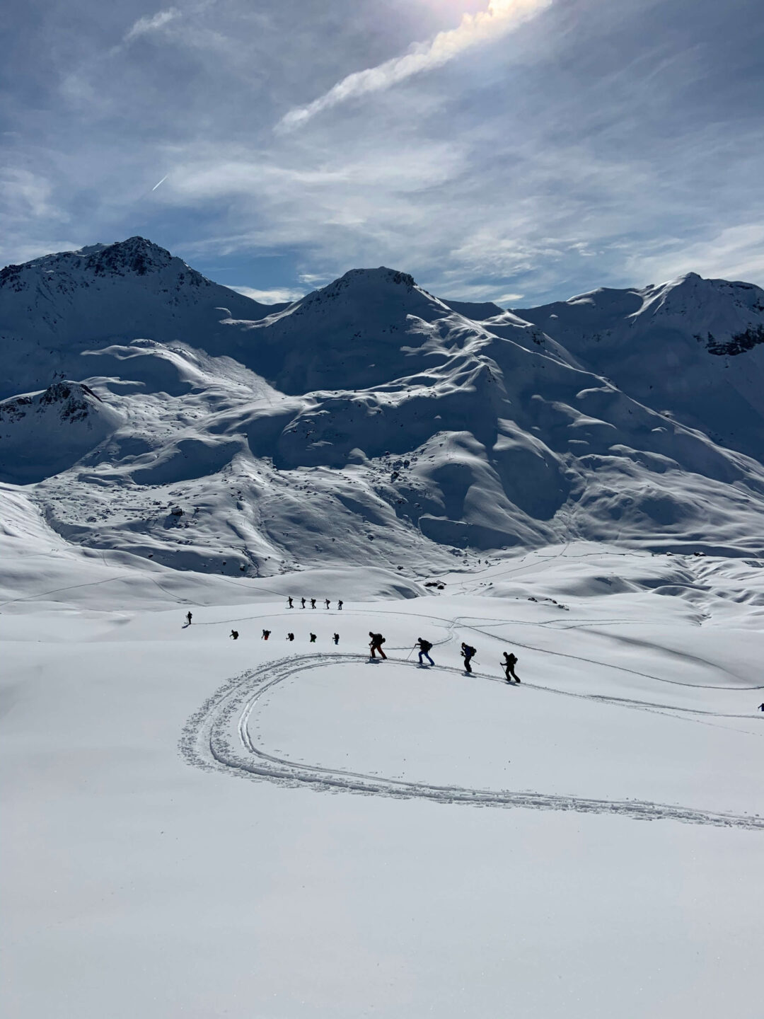 Group of women cross-country skiing on snow tracks through mountain terrain under a cloudy sky
