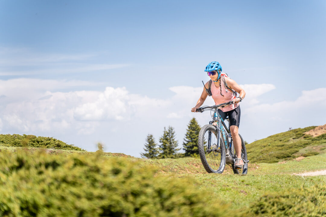 Woman mountain biking on a grassy hillside under a blue sky