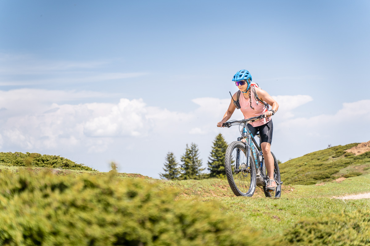 Woman mountain biking on a grassy hillside under a blue sky