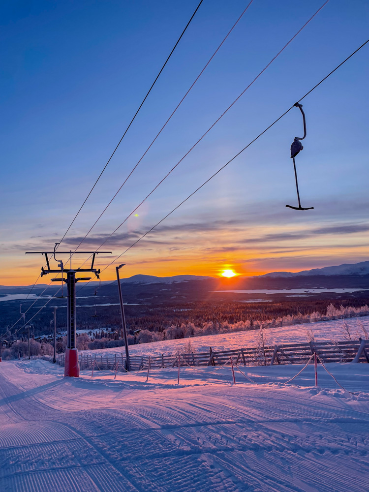 Ski chairlift over snowy downhill slopes at sunset in Sweden.