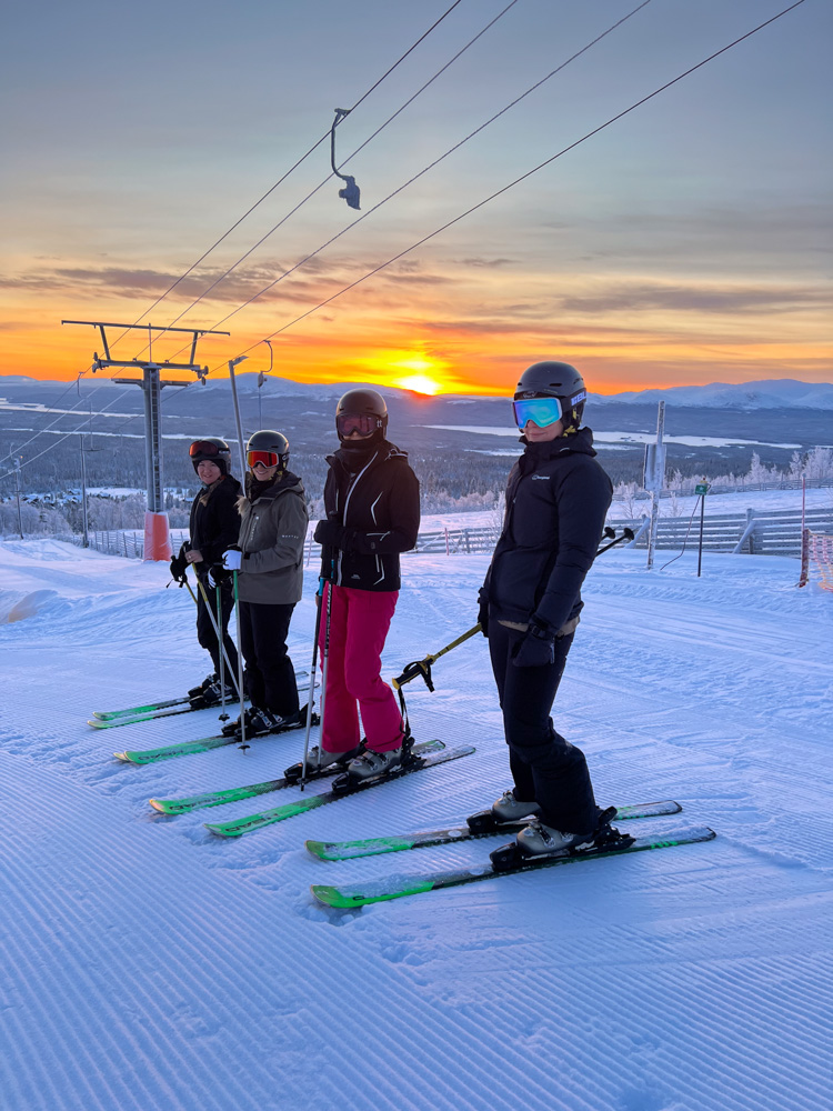 Women skiers with equipment on a snowy piste at a ski resort at sunset