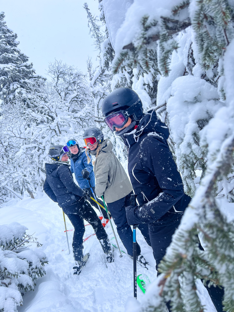 Women skiing in a snowy forest, wearing helmets and goggles on downhill skis
