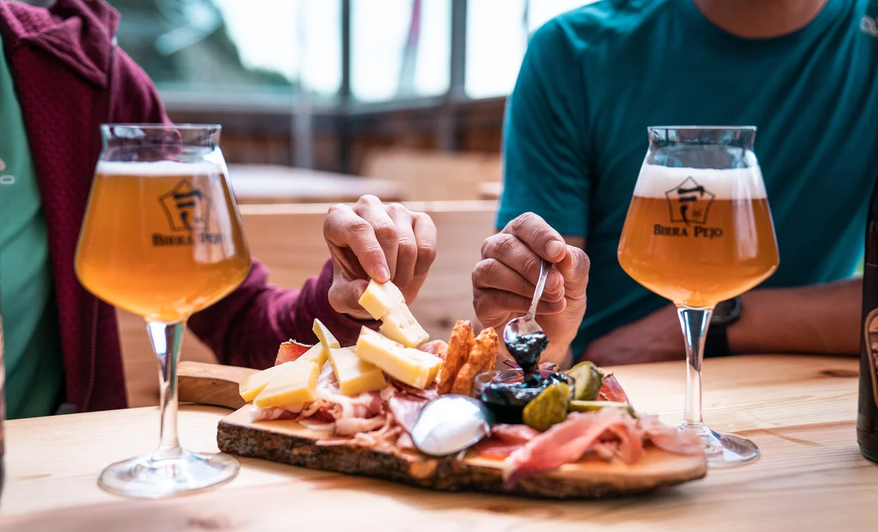 Women sharing a snack on a wooden table with two glasses of beer in an indoor restaurant setting