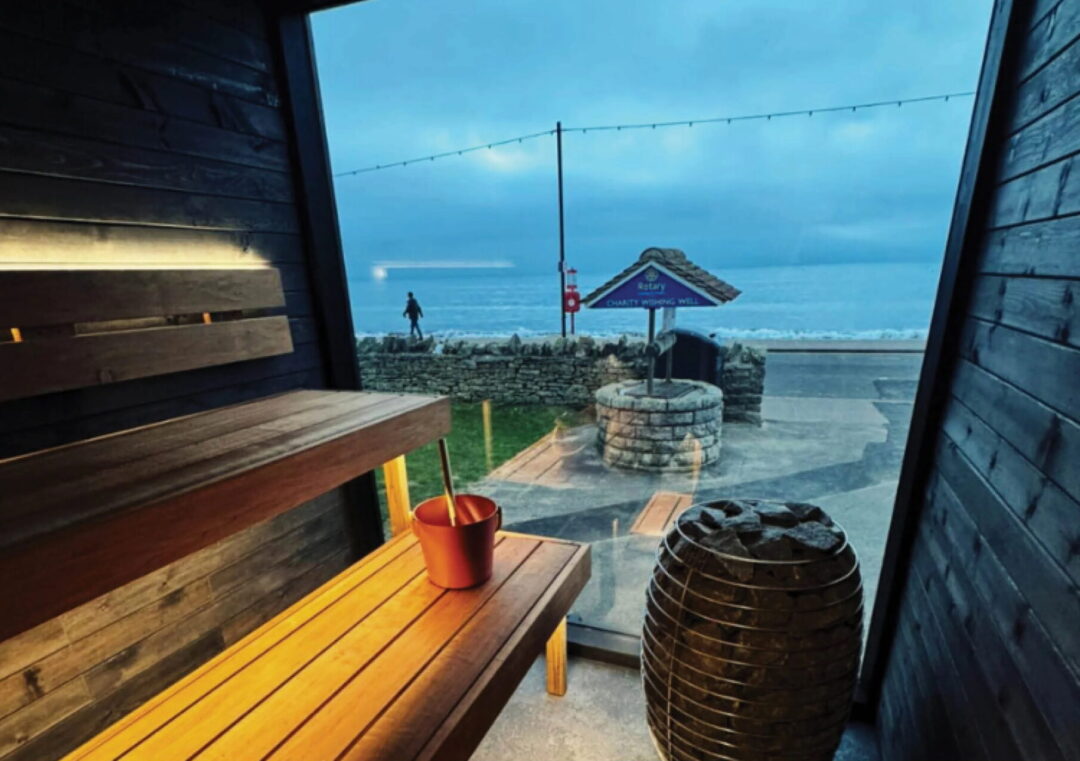 Sauna interior with wooden bench and bucket, overlooking the sea in the UK