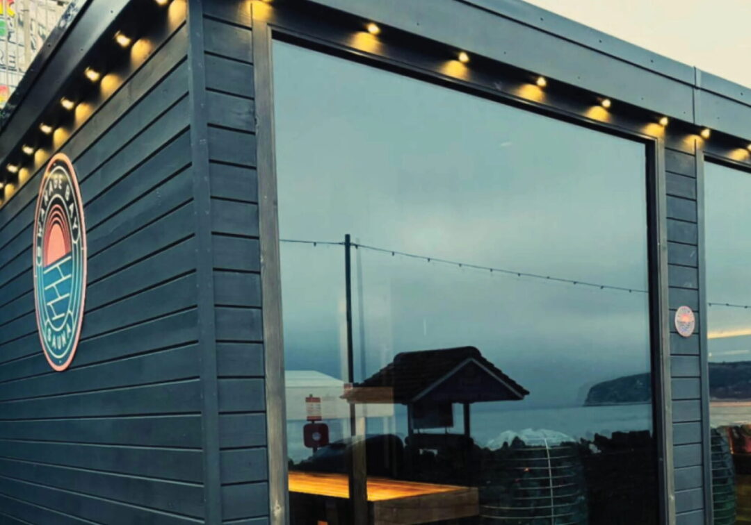 Sauna building exterior with circular logo and warm lights, UK by the window entrance.