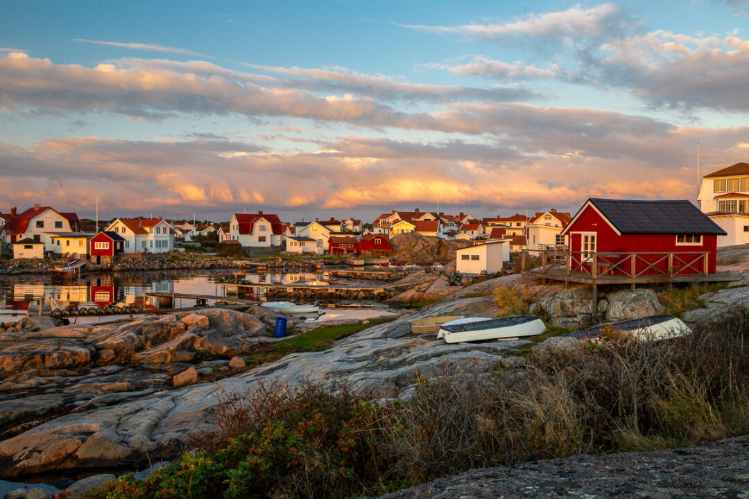 Coastal village at sunset with rocky shoreline, houses and boats along the water