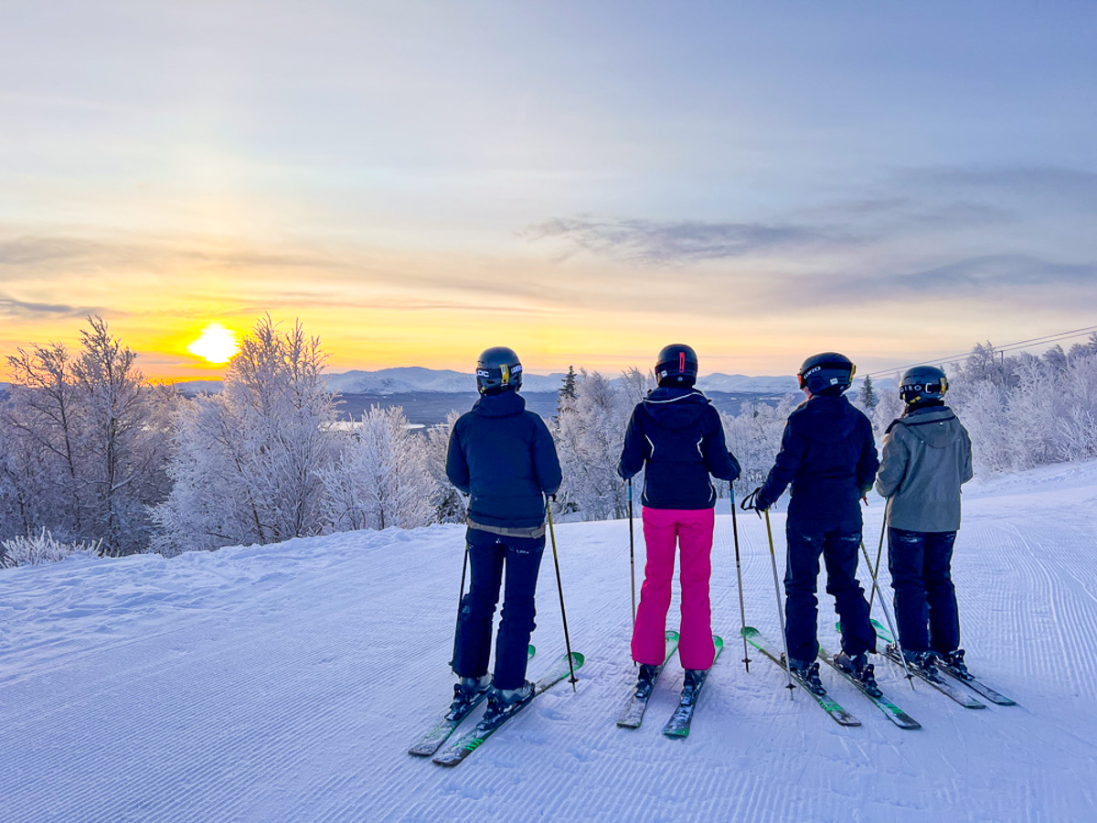 Women standing on skis on a snowy ski slope at sunrise, overlooking a winter landscape