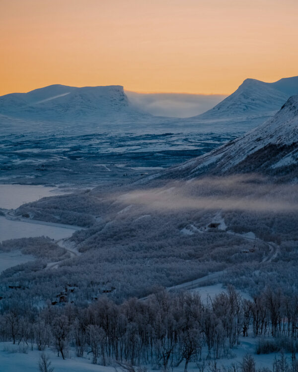 Snow-covered mountain valleys at dusk with winding roads and low mist in winter landscape