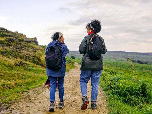 Two women hiking along a scenic countryside footpath with backpacks