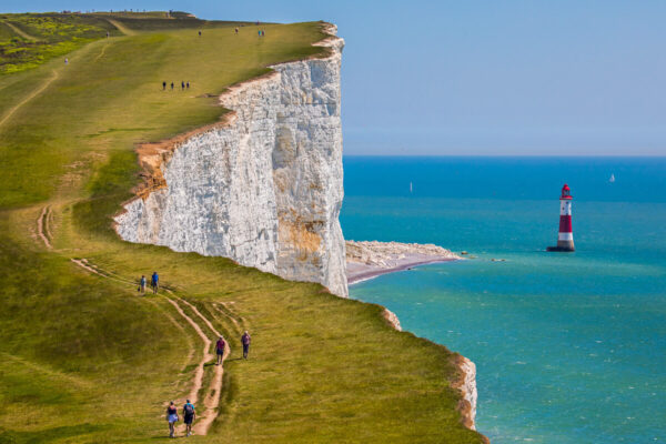 Women hiking on white chalk cliffs by a lighthouse on the UK coast