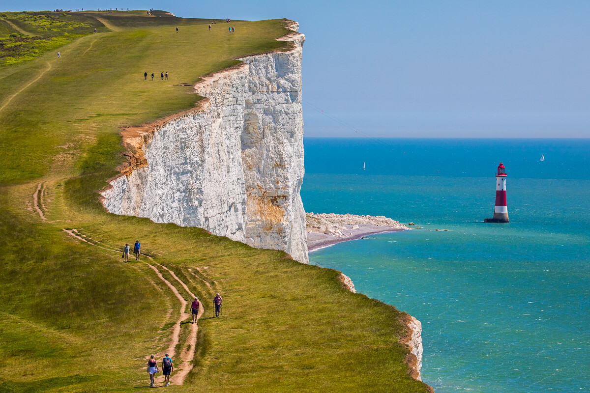 Women hiking on white chalk cliffs by a lighthouse on the UK coast