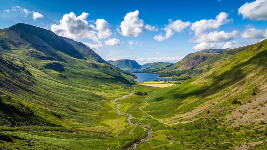 Mountain valley with a winding river flowing through lush green hills under blue sky with clouds