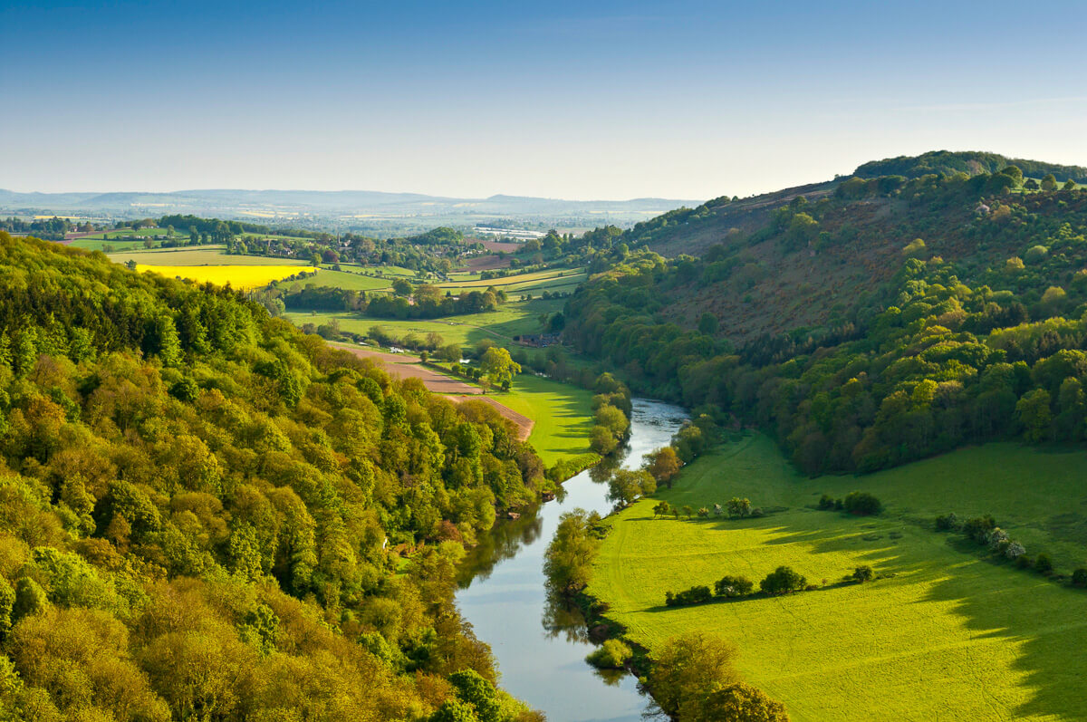Winding river running through lush green countryside valley, aerial view of rolling hills and fields