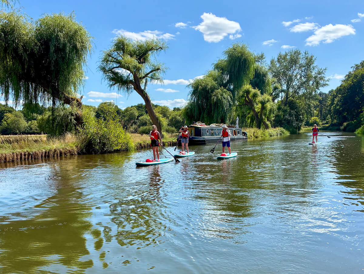 Women paddleboarding on a calm river with lush trees in the background