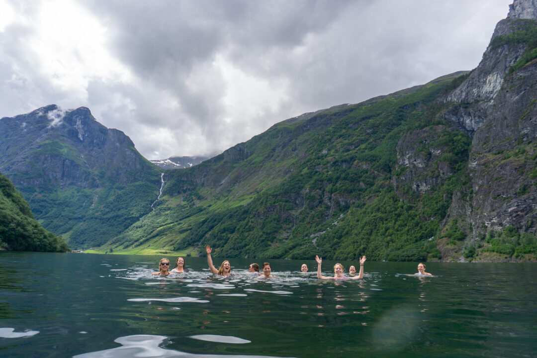 Women swimming in a mountain fjord, with heads and arms above the water under cloudy skies