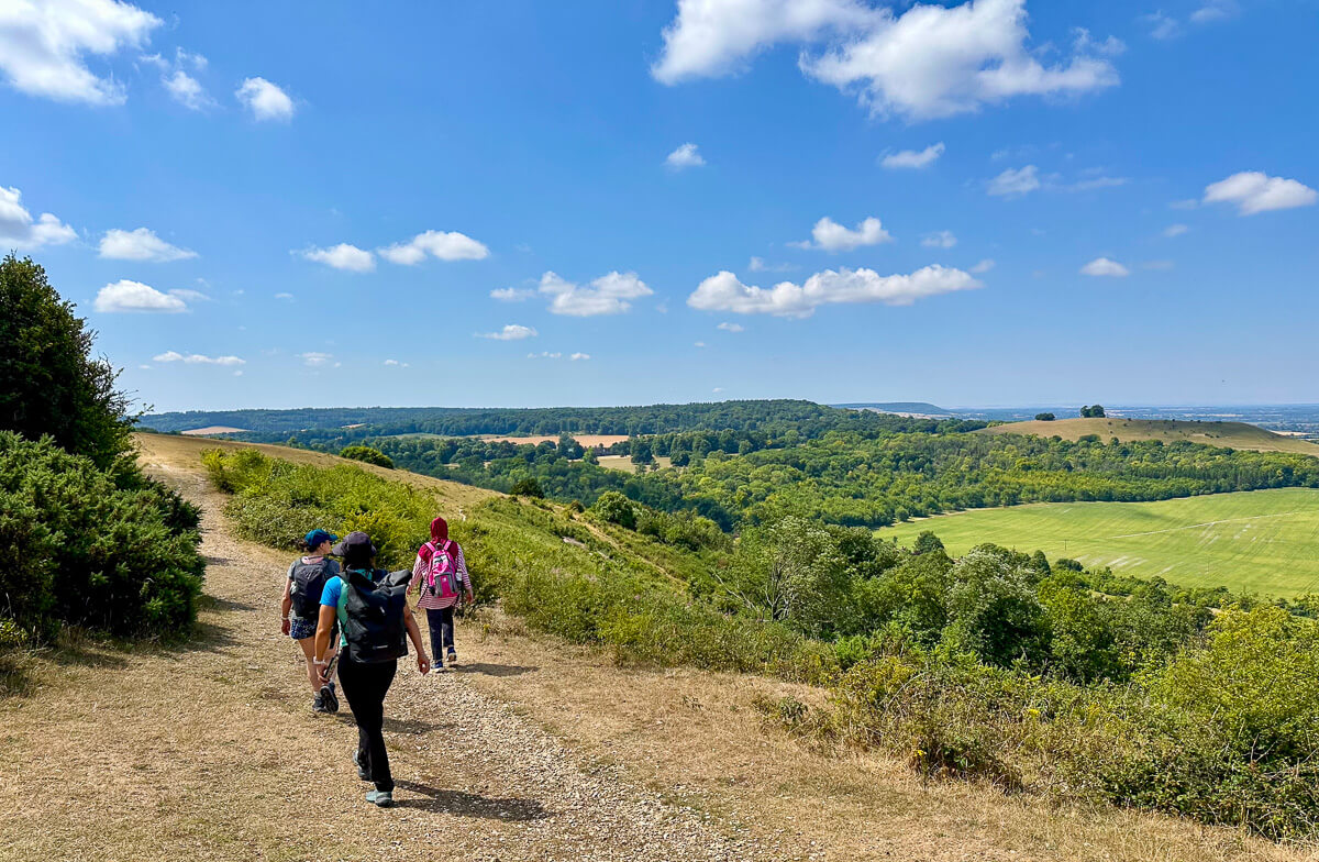 Women hiking along a countryside trail with views over green valleys under a blue sky
