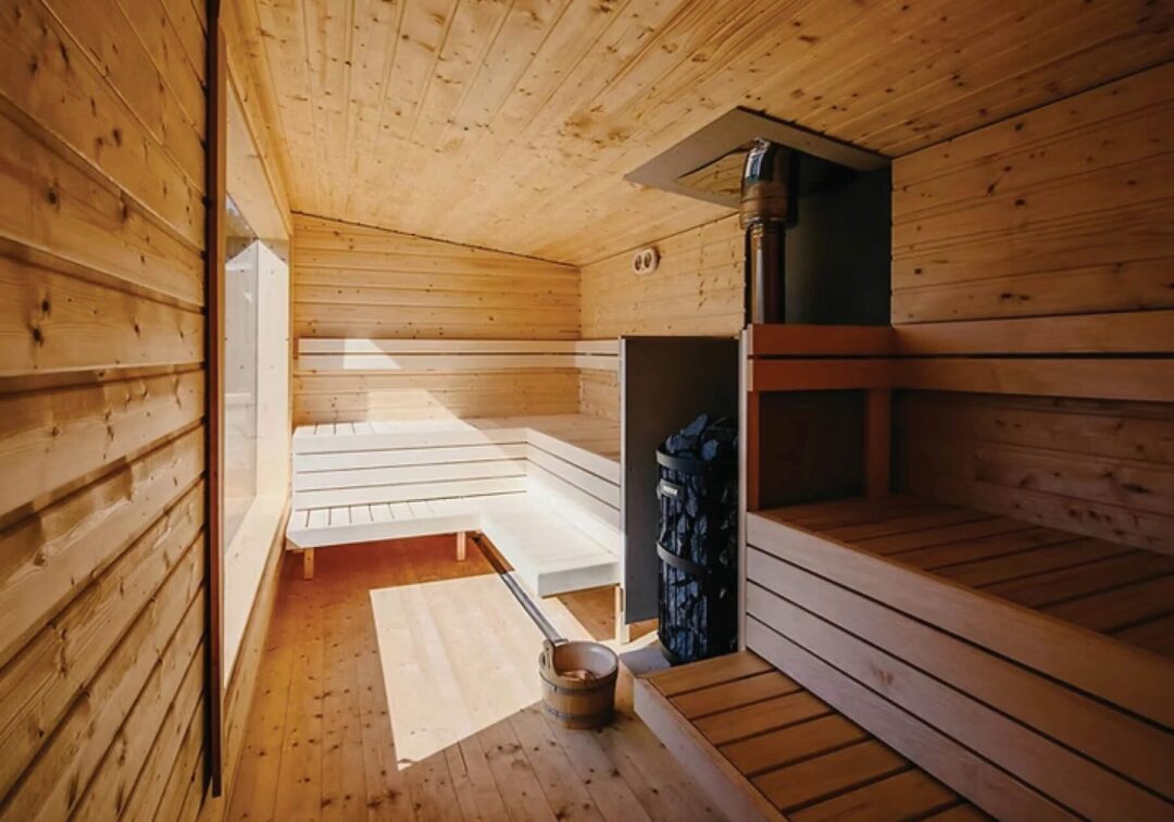Indoor wooden sauna room with bench seating and stove heater, with tiled steps and floor