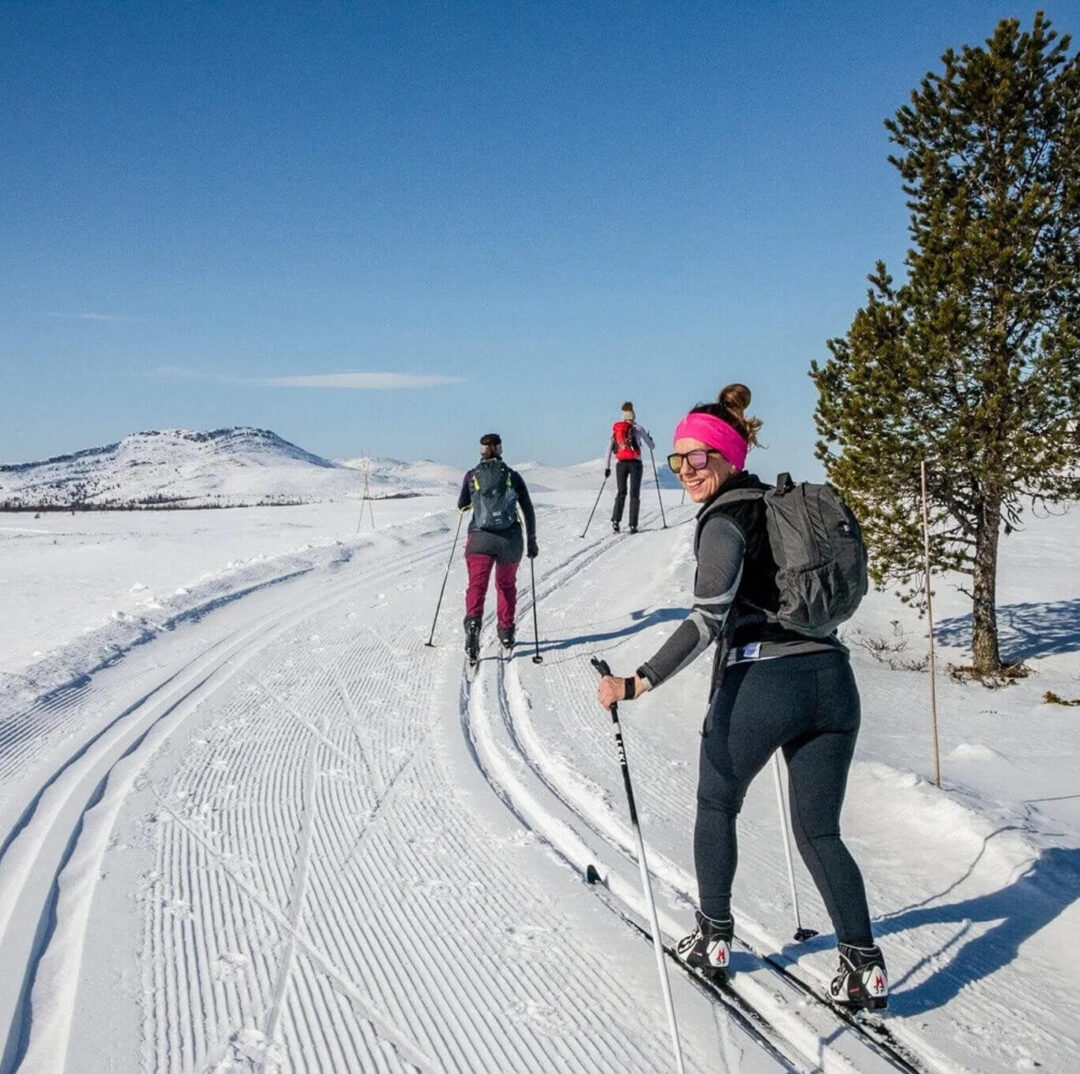Woman cross-country skiing on a snowy mountain trail under a clear blue sky
