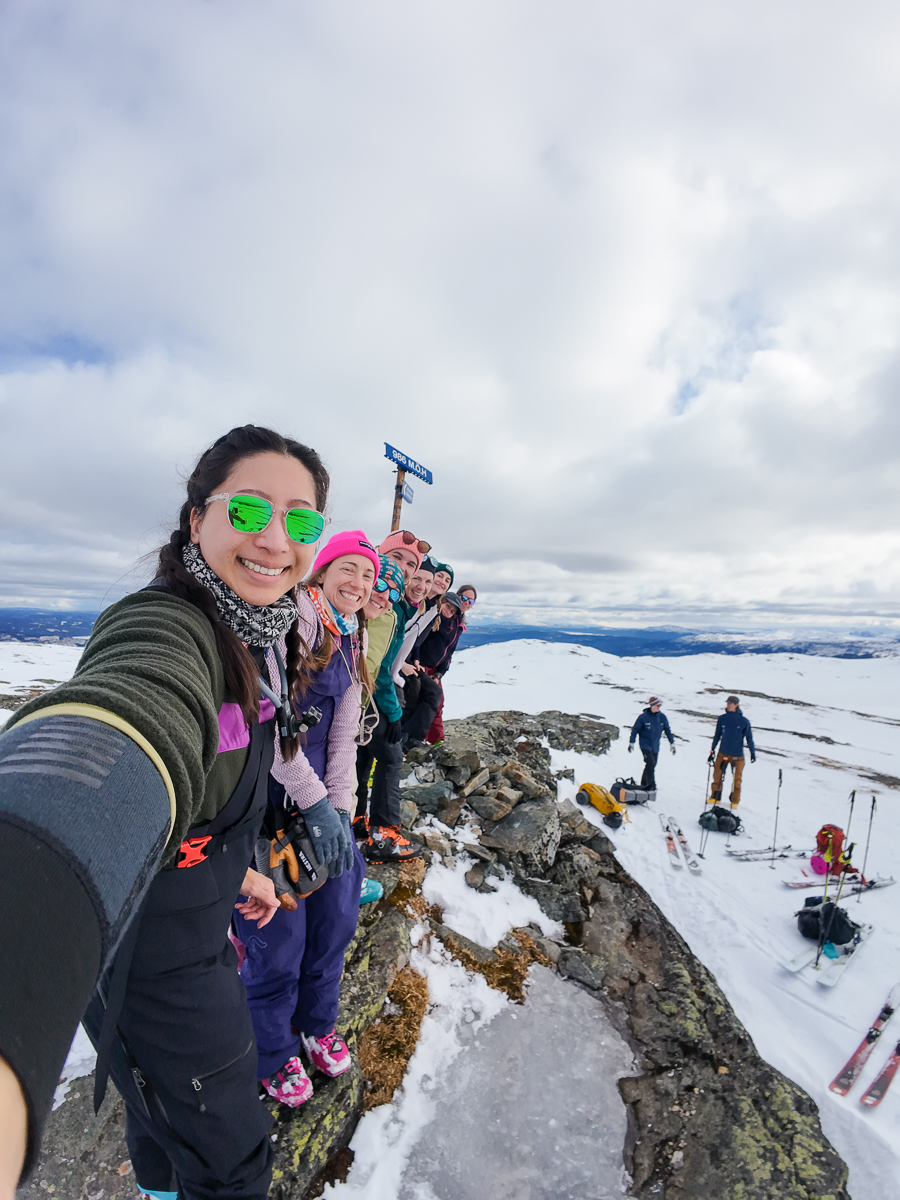 Women smiling on a snowy ski hike on a mountain ridge, with skiers in the background