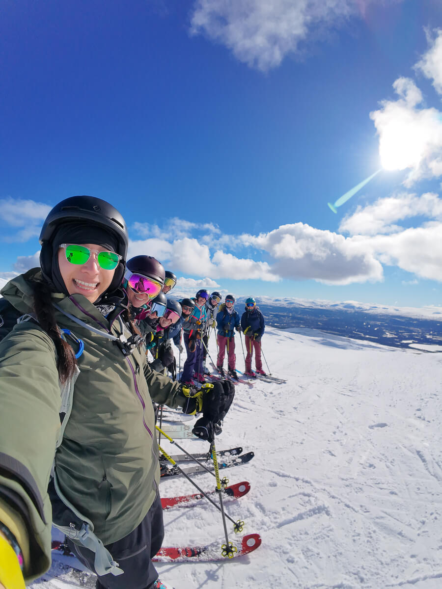 Women skiing on snowy mountain slopes in winter sports gear under a clear blue sky, with a group behind