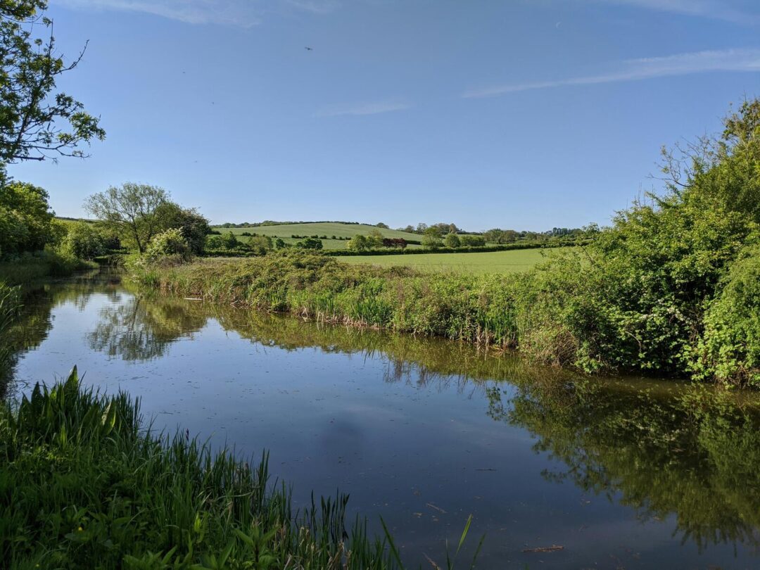 English countryside river winding through green fields and trees under a blue sky