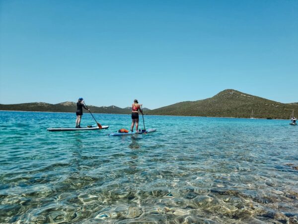 Women paddleboarding (SUP) in clear sea off Croatia’s coast, with mountains in the background.