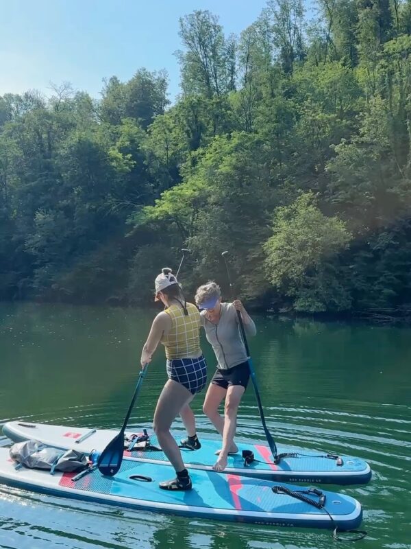 Women paddle boarding on a stand-up paddleboard on a calm river surrounded by trees, Slovenia.
